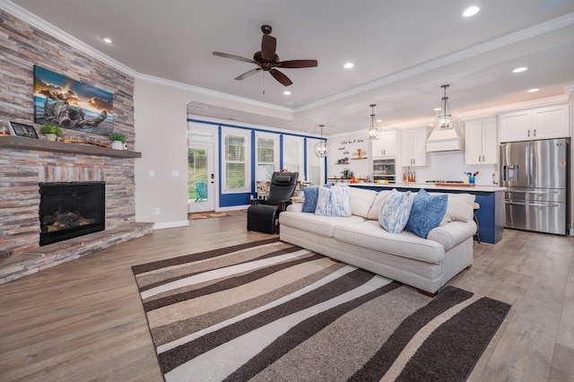 living room with ceiling fan, light hardwood / wood-style floors, a stone fireplace, and ornamental molding