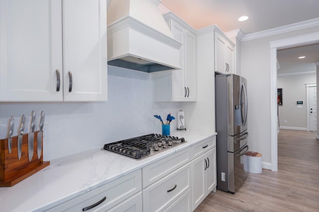 kitchen featuring light stone countertops, appliances with stainless steel finishes, premium range hood, crown molding, and white cabinets