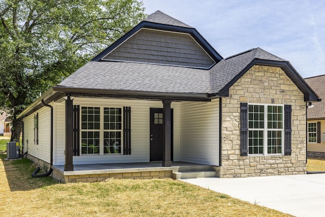 view of front facade featuring central air condition unit, covered porch, and a front yard