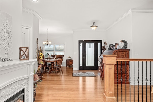 foyer entrance featuring light hardwood / wood-style floors, an inviting chandelier, crown molding, and a stone fireplace