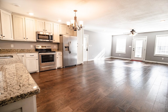 kitchen with dark wood-type flooring, light stone counters, decorative light fixtures, ceiling fan with notable chandelier, and appliances with stainless steel finishes