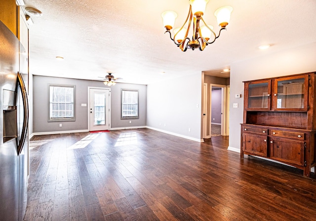 unfurnished living room with a textured ceiling, ceiling fan with notable chandelier, and dark wood-type flooring