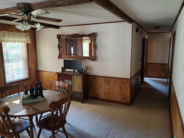 unfurnished dining area featuring light carpet, a textured ceiling, ceiling fan, crown molding, and beam ceiling