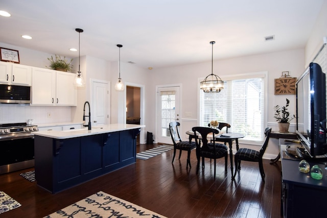 kitchen featuring a center island with sink, a kitchen breakfast bar, white cabinets, appliances with stainless steel finishes, and decorative light fixtures