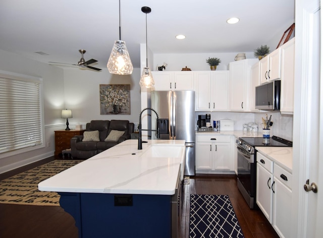 kitchen with white cabinets, a center island with sink, dark hardwood / wood-style floors, appliances with stainless steel finishes, and decorative light fixtures