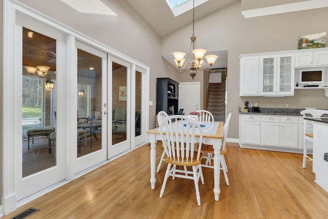 dining space with high vaulted ceiling, light wood-type flooring, and an inviting chandelier