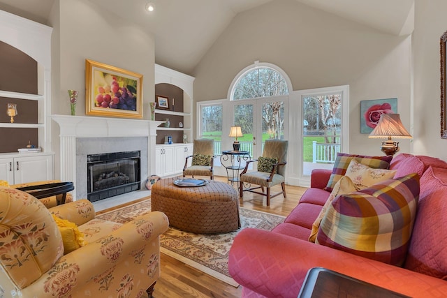 living room featuring a tile fireplace, built in features, high vaulted ceiling, and wood-type flooring