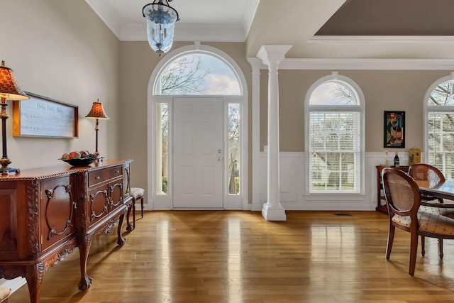 foyer with a notable chandelier, light wood-type flooring, ornate columns, and crown molding