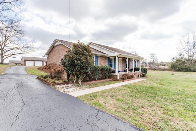 view of front of house featuring covered porch, a garage, a front lawn, and an outdoor structure