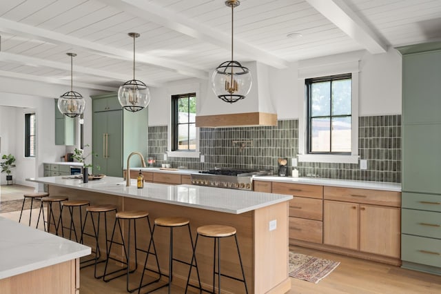 kitchen with light stone counters, backsplash, hanging light fixtures, and a center island with sink