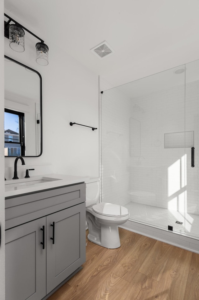 bathroom with toilet, hardwood / wood-style floors, vanity, and an enclosed shower