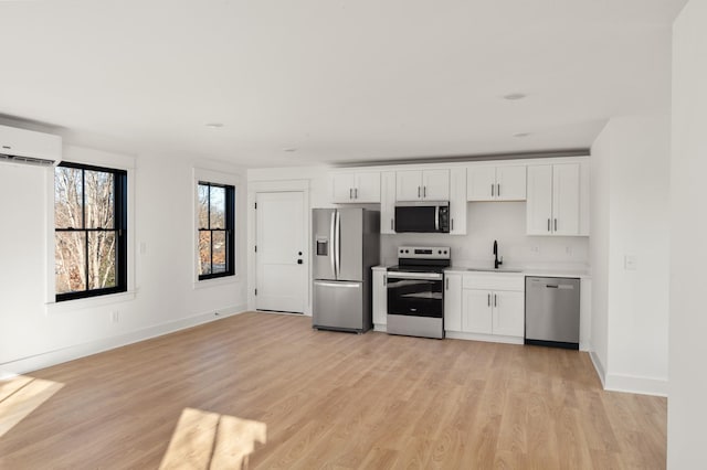 kitchen featuring white cabinets, stainless steel appliances, light hardwood / wood-style floors, sink, and a wall unit AC