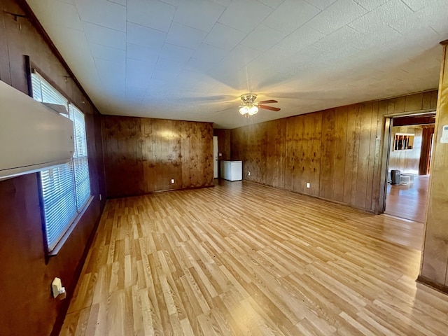 unfurnished living room featuring ceiling fan, wood walls, and light hardwood / wood-style flooring