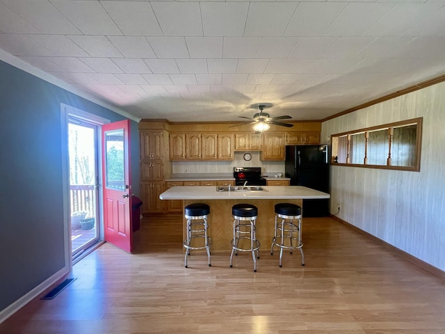 kitchen featuring light wood-type flooring, ornamental molding, a breakfast bar, black appliances, and a center island with sink