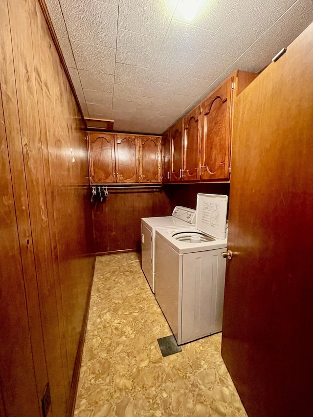 laundry room featuring separate washer and dryer, wood walls, and cabinets