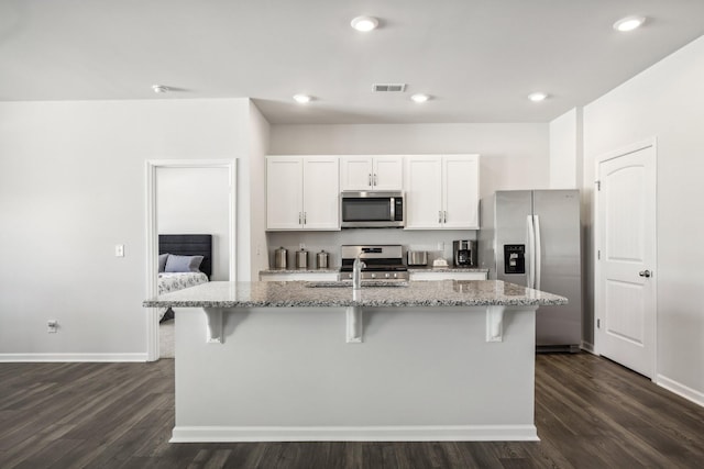 kitchen featuring white cabinets, light stone countertops, an island with sink, and stainless steel appliances