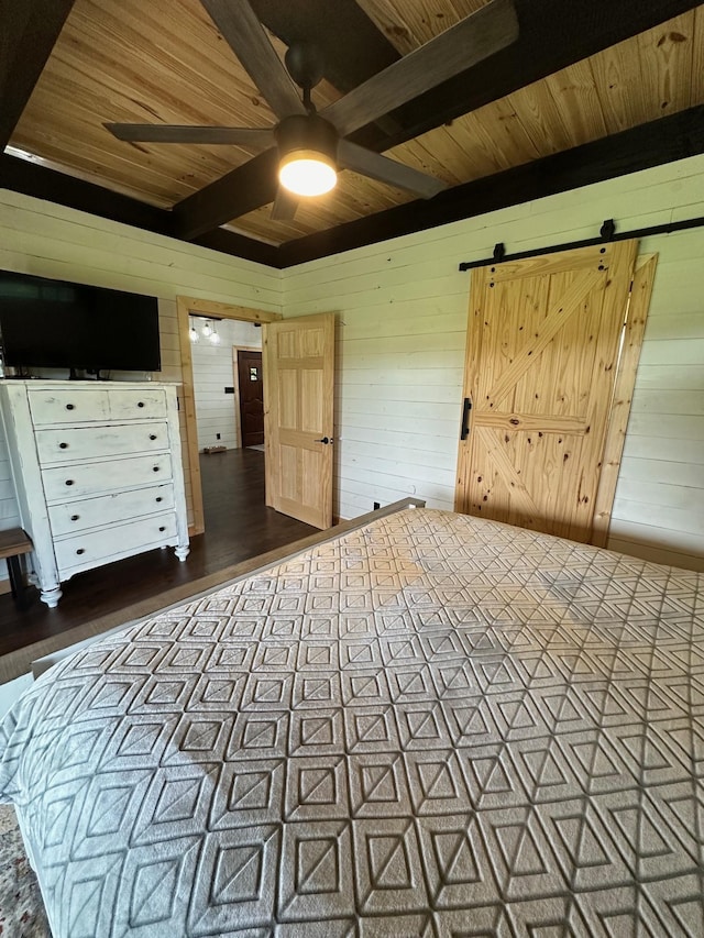 unfurnished bedroom featuring beam ceiling, a barn door, dark hardwood / wood-style floors, wood walls, and wood ceiling