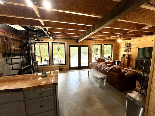 interior space with concrete flooring, beam ceiling, access to exterior, and wooden walls