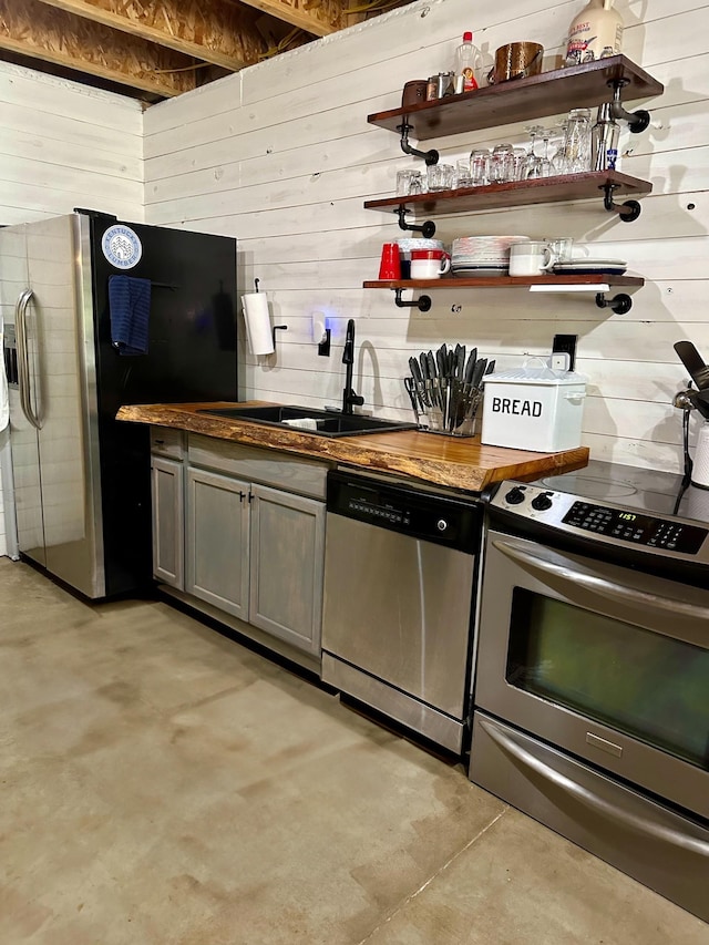 kitchen with gray cabinets, wood walls, sink, and stainless steel appliances