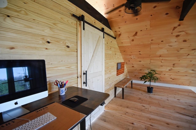 office space featuring a barn door, wooden walls, light hardwood / wood-style floors, and vaulted ceiling