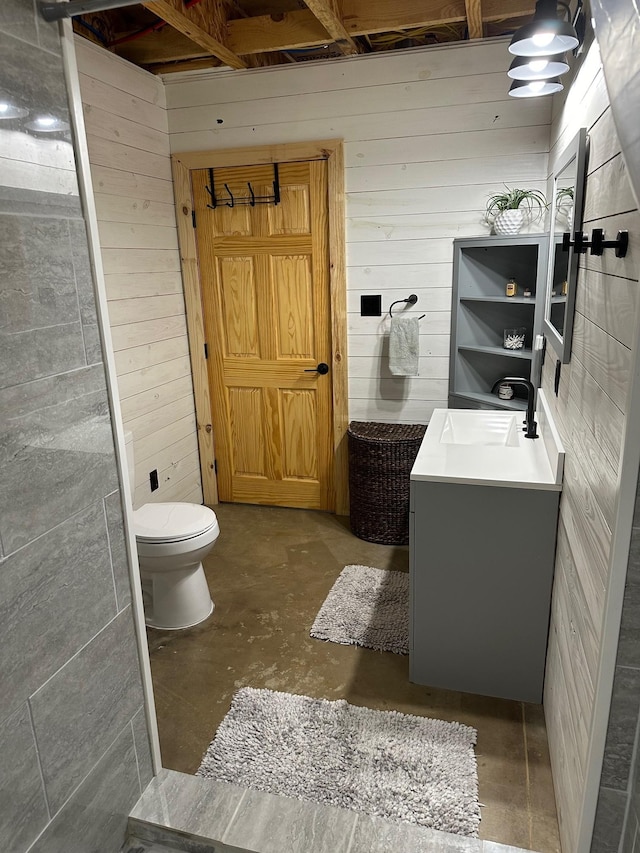 bathroom with vanity, wood walls, toilet, and concrete flooring