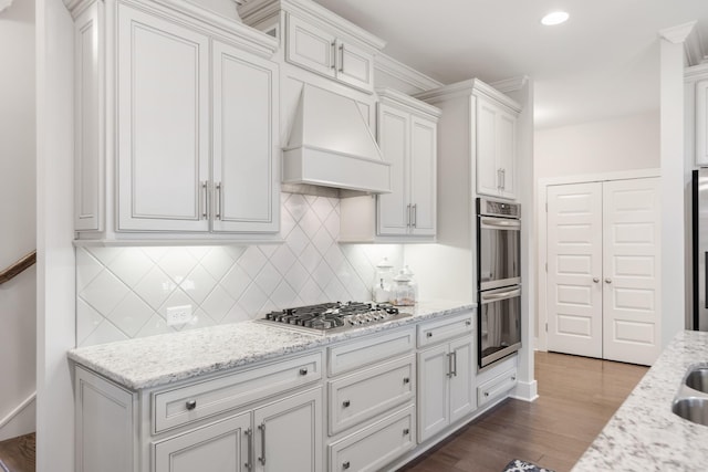 kitchen featuring hardwood / wood-style floors, custom exhaust hood, white cabinets, light stone countertops, and appliances with stainless steel finishes