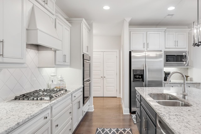 kitchen featuring appliances with stainless steel finishes, custom range hood, sink, white cabinets, and hanging light fixtures