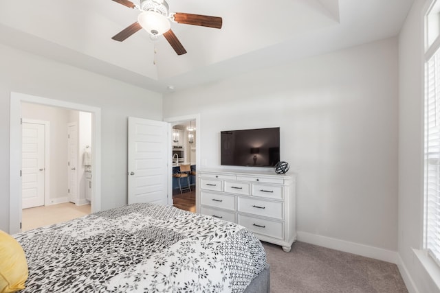 bedroom with ensuite bathroom, ceiling fan, light carpet, and a tray ceiling