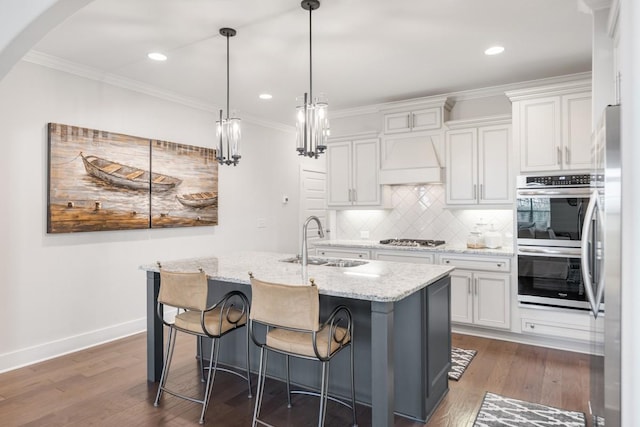 kitchen featuring sink, an island with sink, light stone counters, white cabinetry, and stainless steel appliances