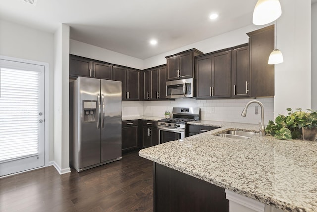 kitchen with light stone counters, sink, pendant lighting, and appliances with stainless steel finishes