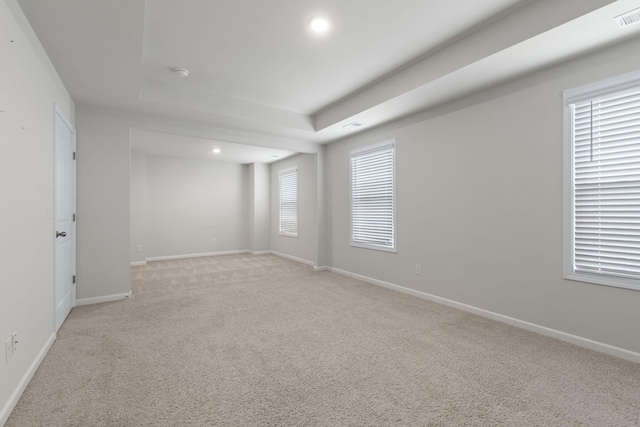 unfurnished room featuring a raised ceiling, a wealth of natural light, and light colored carpet