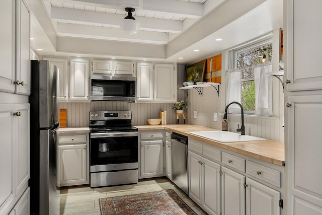 kitchen featuring beam ceiling, sink, white cabinets, and stainless steel appliances