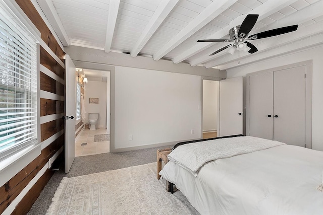 bedroom featuring carpet, ensuite bath, ceiling fan, beamed ceiling, and a closet