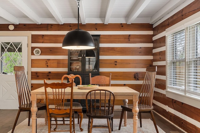 dining area featuring wood walls, beamed ceiling, and a healthy amount of sunlight