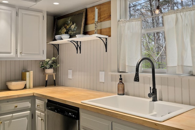 kitchen with stainless steel dishwasher, wood counters, white cabinets, and sink