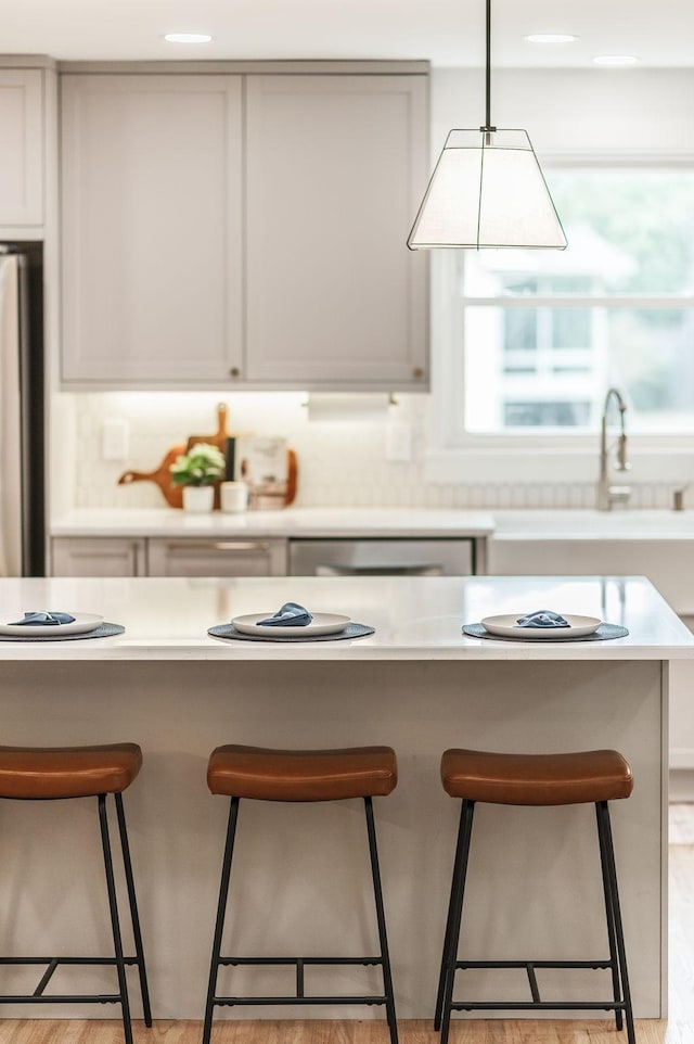 kitchen with a kitchen breakfast bar, stainless steel refrigerator, decorative light fixtures, and light hardwood / wood-style flooring