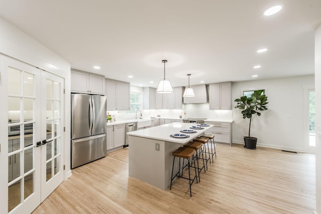 kitchen with appliances with stainless steel finishes, backsplash, custom range hood, pendant lighting, and a center island