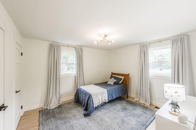 bedroom with a chandelier, wood-type flooring, and multiple windows