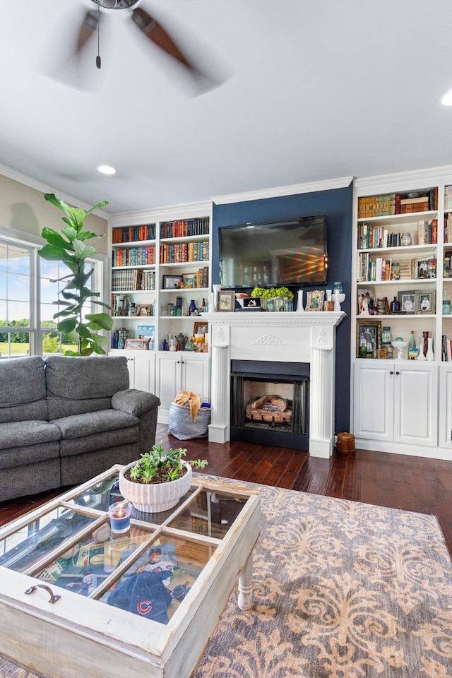 living room with built in shelves, dark hardwood / wood-style floors, ceiling fan, and ornamental molding