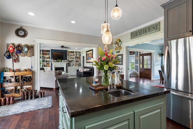 kitchen with green cabinetry, stainless steel refrigerator, a kitchen island with sink, and sink