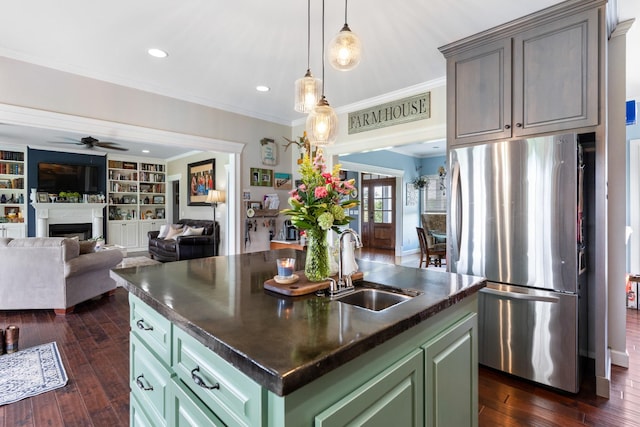 kitchen featuring a kitchen island with sink, sink, green cabinetry, built in shelves, and stainless steel fridge