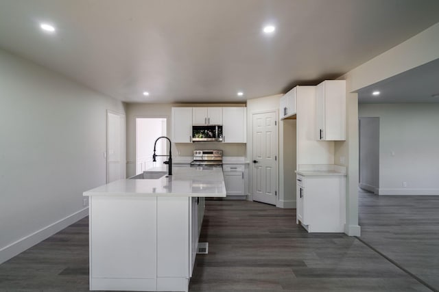 kitchen featuring white cabinets, sink, an island with sink, appliances with stainless steel finishes, and dark hardwood / wood-style flooring