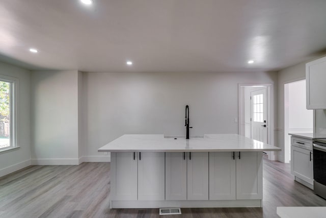 kitchen featuring white cabinets, light stone counters, and an island with sink