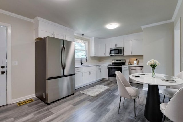 kitchen with sink, hanging light fixtures, stainless steel appliances, crown molding, and white cabinets