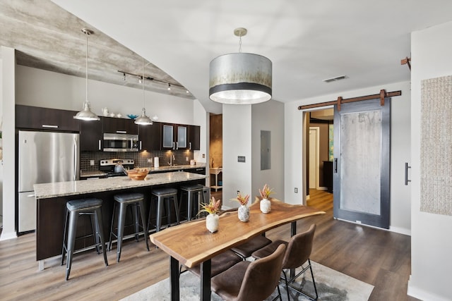 dining area featuring electric panel, sink, rail lighting, a barn door, and wood-type flooring