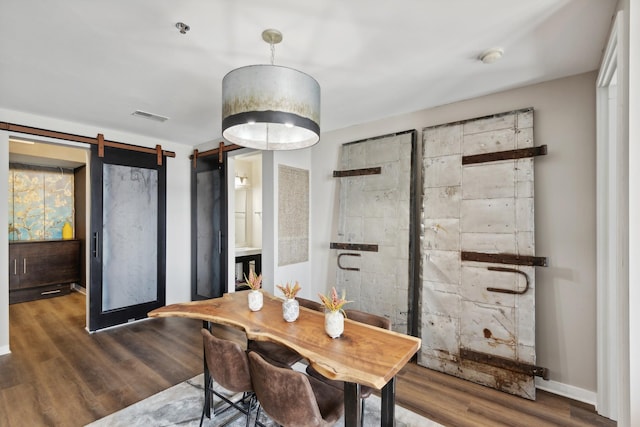 dining room with a barn door and dark hardwood / wood-style floors