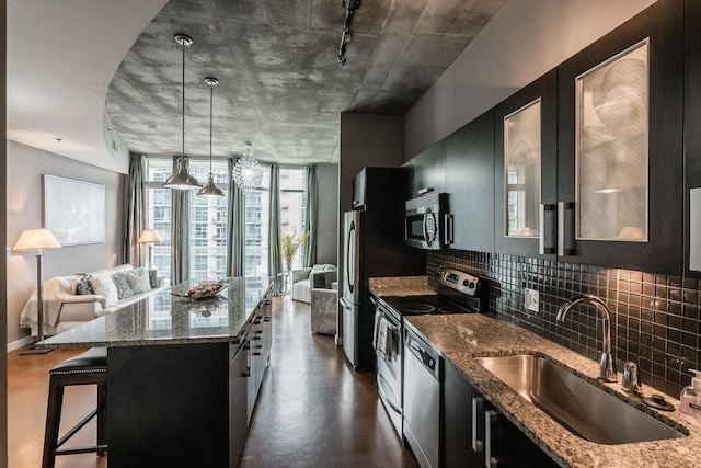 kitchen featuring appliances with stainless steel finishes, dark stone counters, sink, a kitchen island, and hanging light fixtures