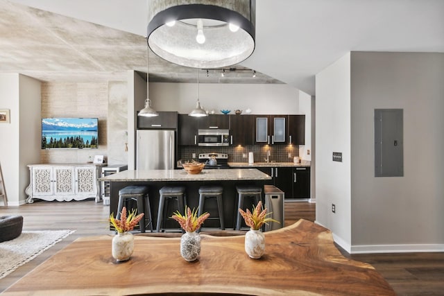 kitchen featuring a kitchen bar, backsplash, stainless steel appliances, electric panel, and a kitchen island