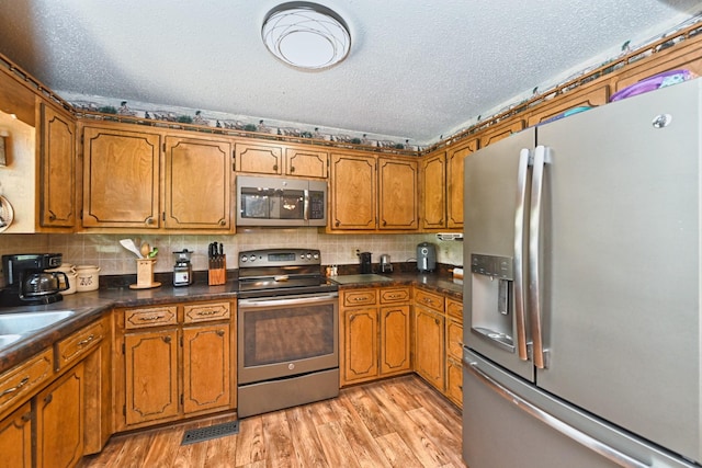 kitchen featuring a textured ceiling, stainless steel appliances, light hardwood / wood-style flooring, and decorative backsplash