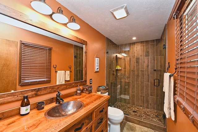 bathroom with a textured ceiling, a shower with door, vanity, and toilet